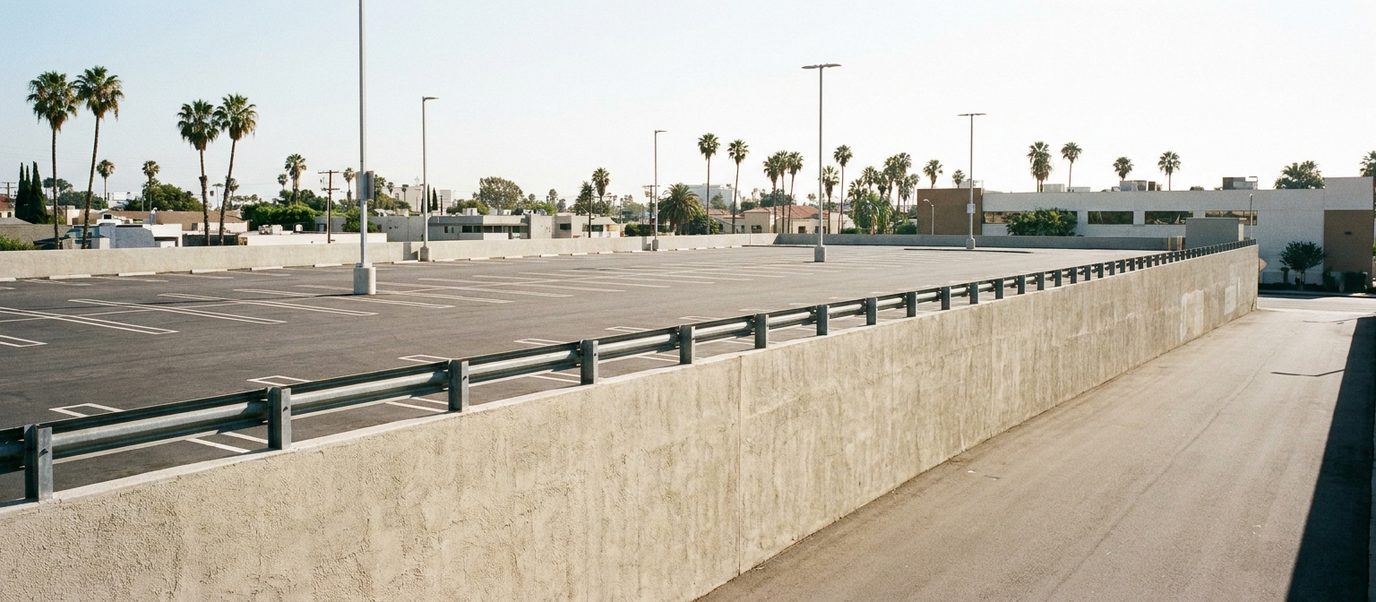 Long poured concrete parking lot retaining wall with guardrail holding a commercial lot above an access road in Los Angeles