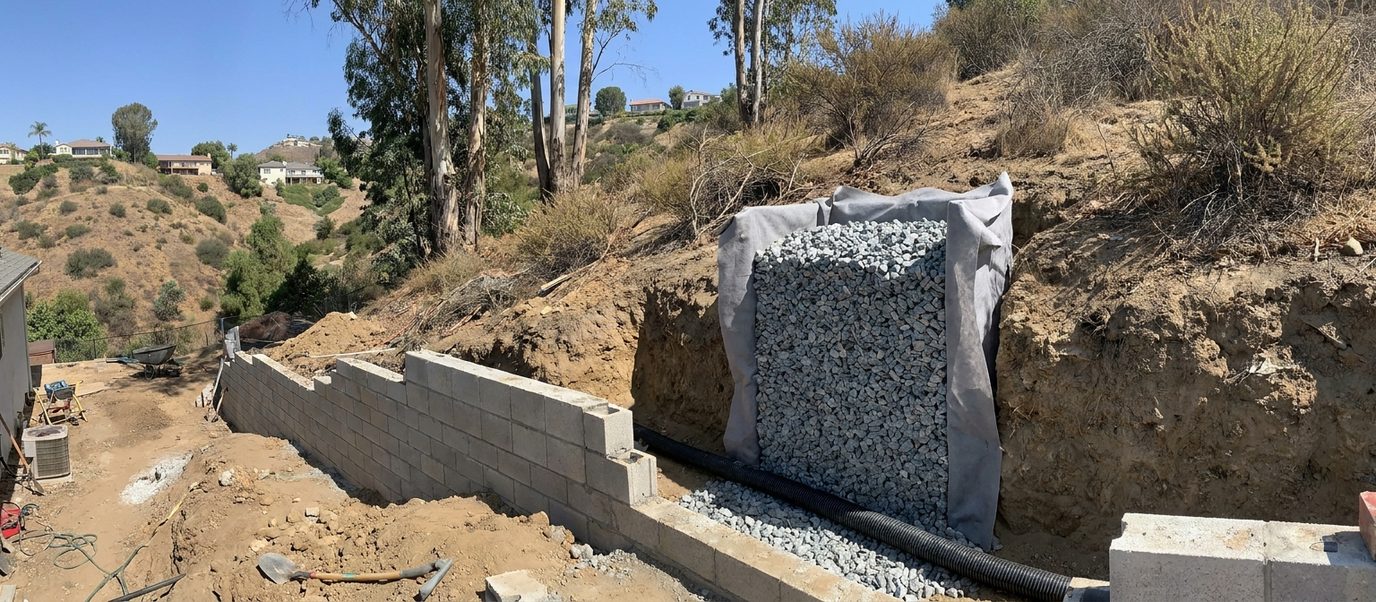 Gravel drainage chimney wrapped in filter fabric with a perforated pipe behind a retaining wall under construction in Los Angeles