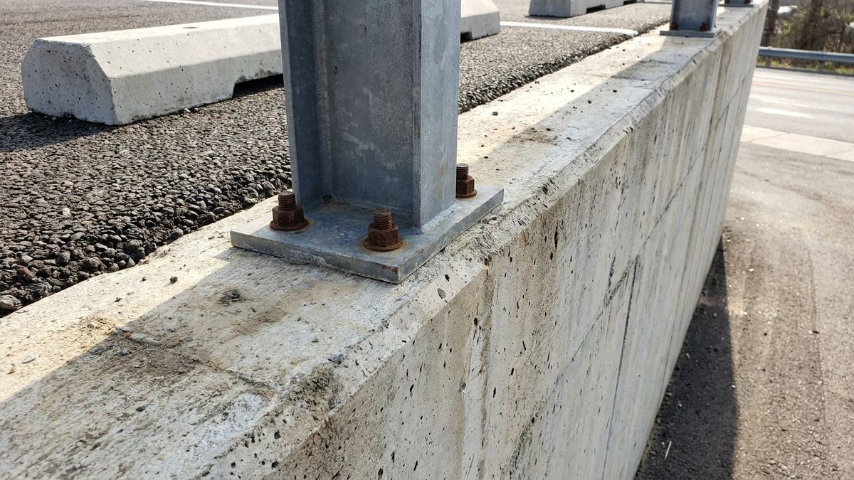 Guardrail post base plate bolted into the top of a poured concrete parking lot retaining wall in Los Angeles