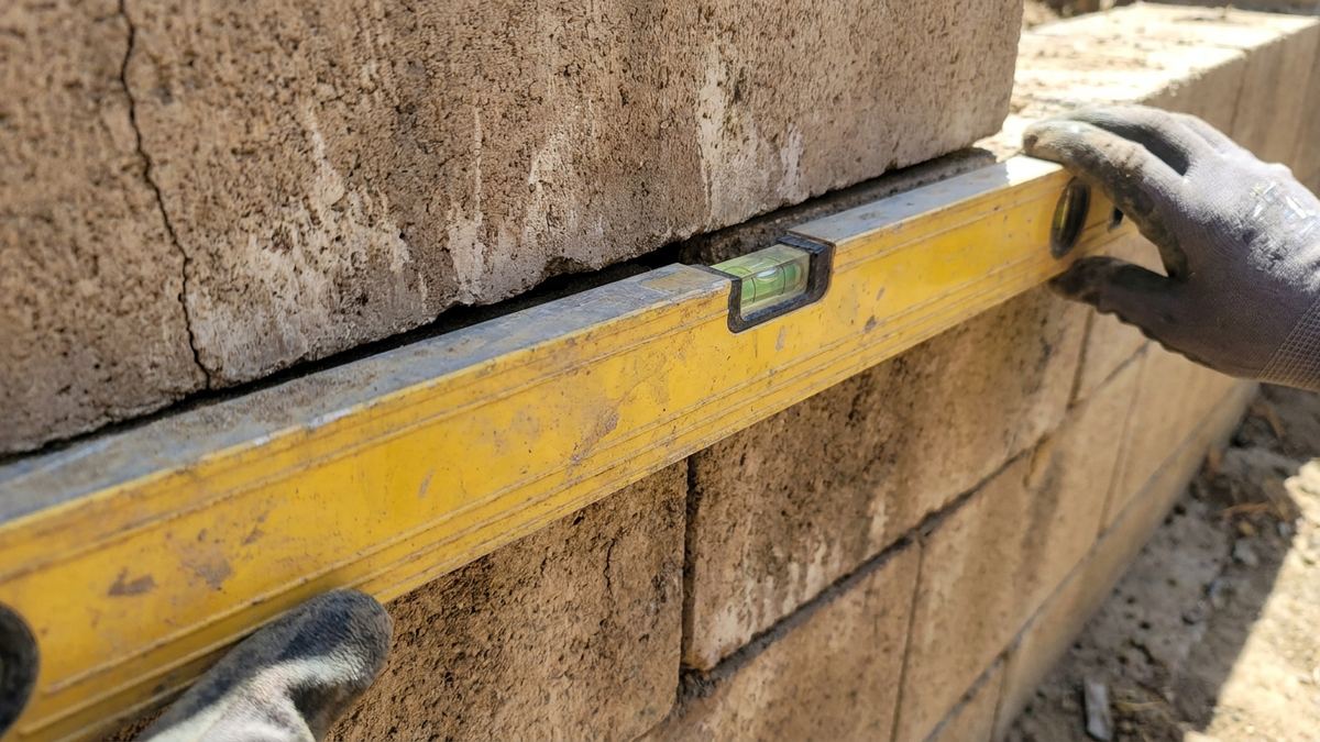 Spirit level held against a tilted block retaining wall showing a clear gap at the top where the wall has moved out of plumb