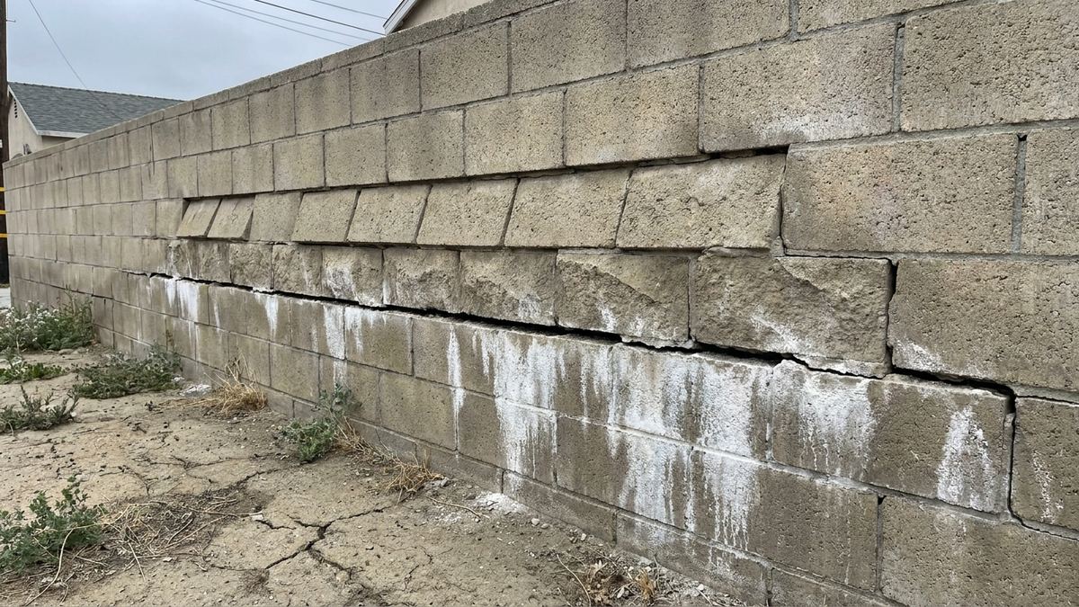 Horizontal crack running along a block retaining wall with the courses above pushed outward and efflorescence staining below